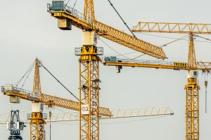 Services Cluster of yellow tower cranes at a construction site with a gloomy sky background.